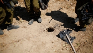 Israeli soldiers stand next to a hole in the ground they suspect is connected to a tunnel, outside the Gaza Strip